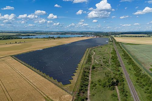 Blick auf großen Solarpark und Grünflächen, im Hintergrund ein See