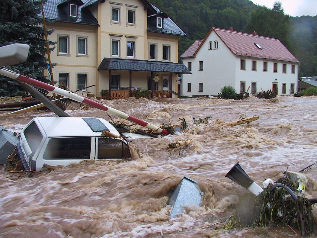 Ein Auto und weitere Teile werden durch braune Fluten mitgerissen. 