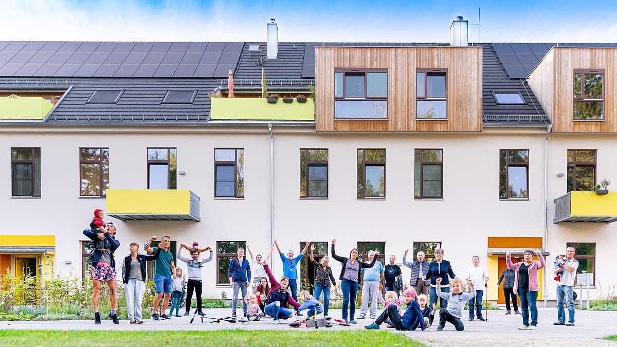 Menschen vor Mehrfamilienhaus mit Photovoltaik in Weimar