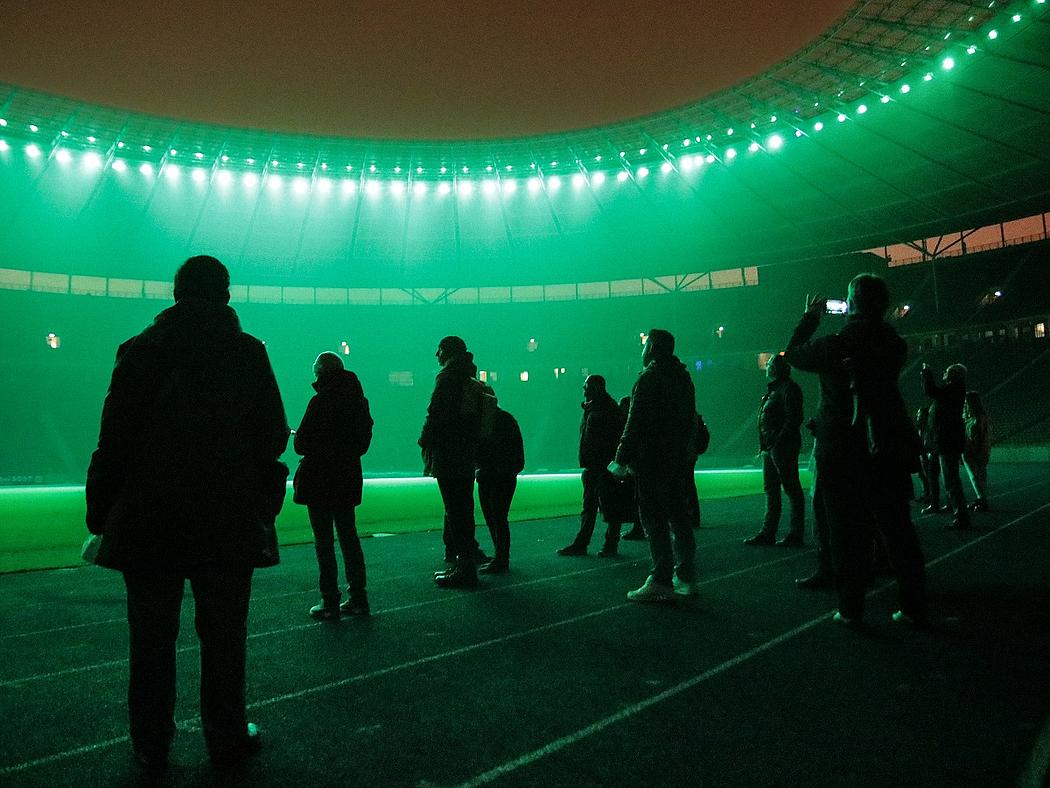 Menschengruppe im Olympiastadion bei Nacht mit grüner Beleuchtung