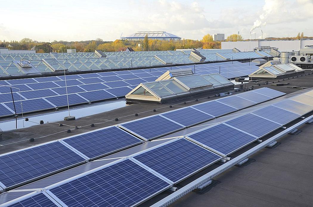Photovoltaikanlage auf einem Dach. Im Hintergrund ist ein Fußballstadion zu sehen.