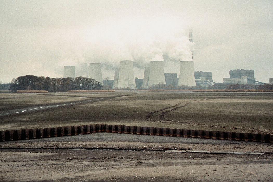 Blick über verdorrte Landschaft auf ein Kraftwerk mit rauchenden Schornsteinen