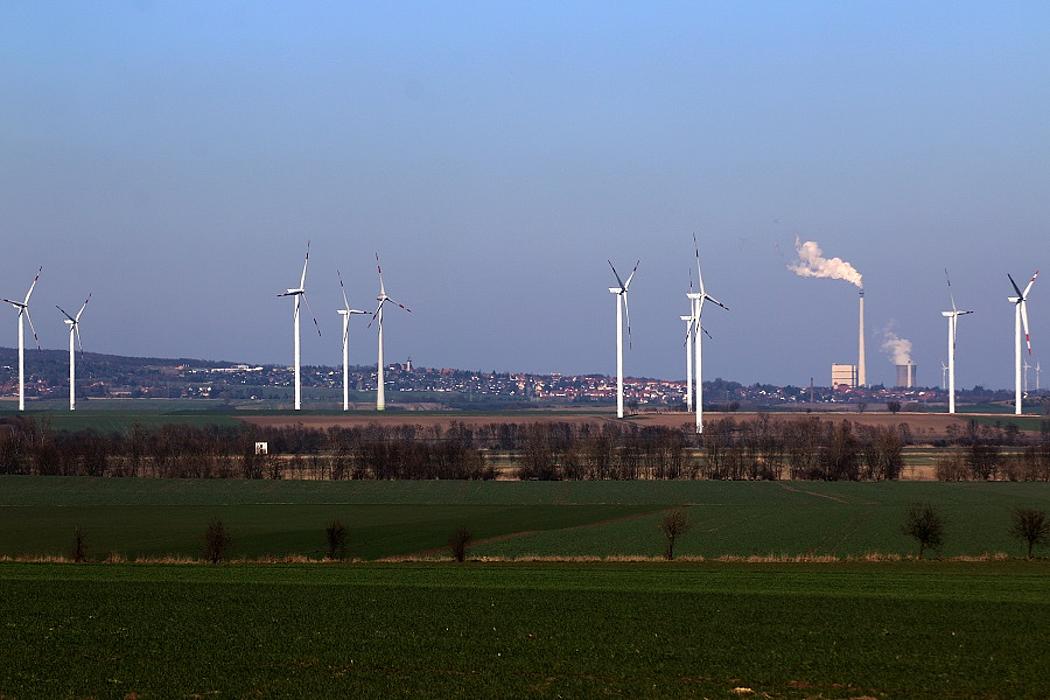 Windpark auf freiem Feld, im Hintergrund ein Kohlekraftwerk