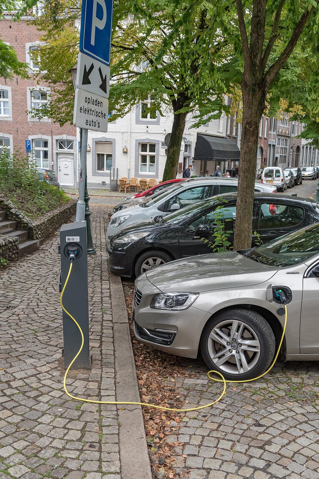 silbernes E-Auto beim laden an einer Säule. Darüber ein Schild, auf dem steht: "opladen elektrische autos"