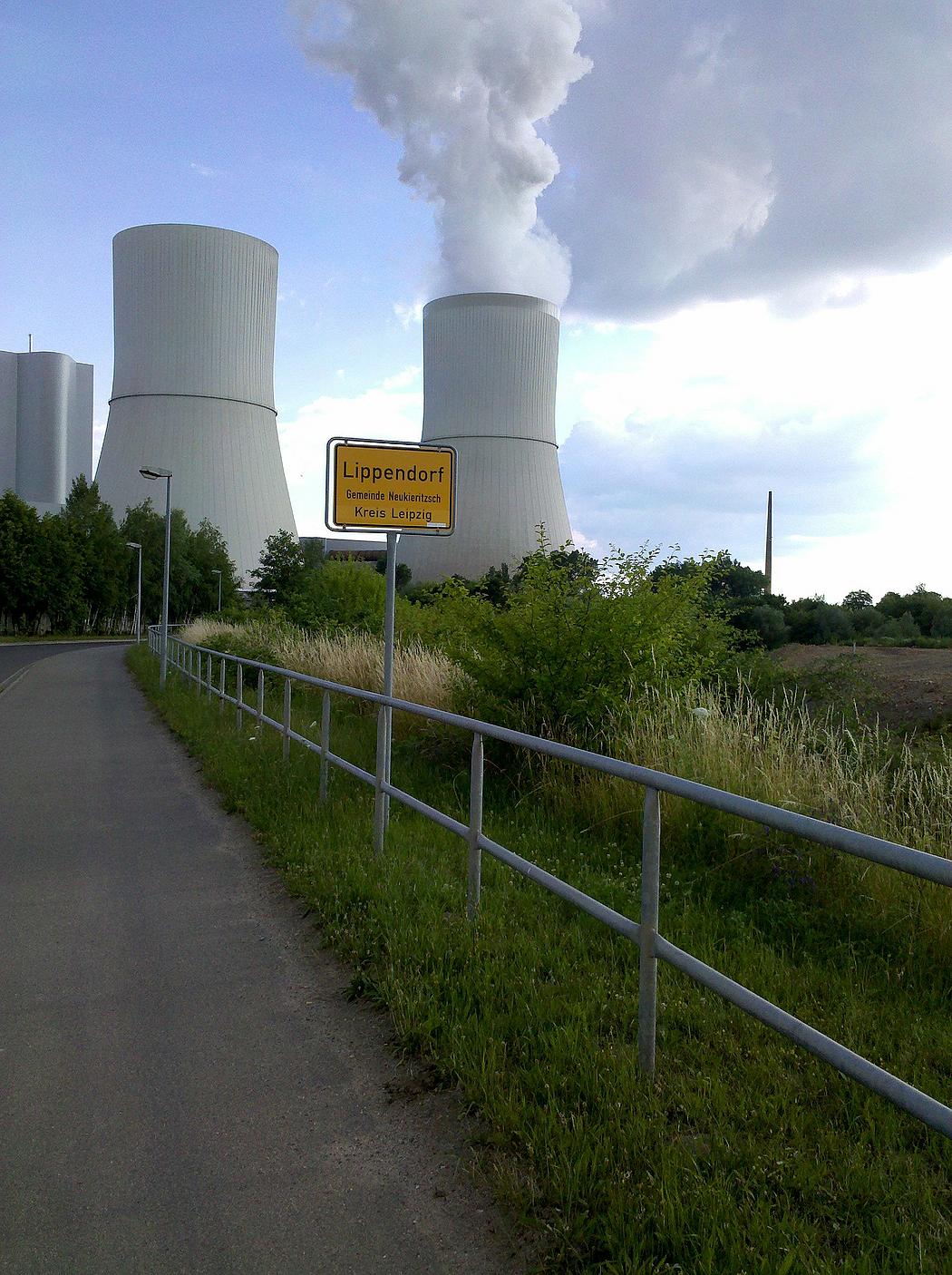 Ortsschild von Lippendorf im Kreis Leipzig. Im Hintergrund die rauchenden Kühltürme des örtlichen Braunkohlekraftwerks.