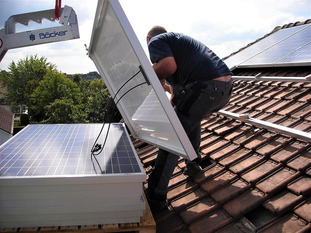 Mann installiert Solarmodule auf einem Hausdach