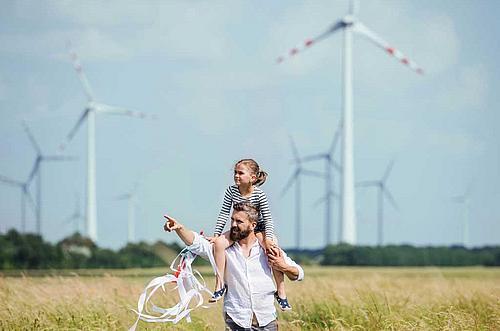 Mann mit Kind auf der Schulter in einem Kornfeld, im Hintergrund Windkraftanlagen