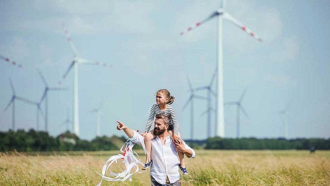 Mann mit Kind auf der Schulter in einem Kornfeld, im Hintergrund Windkraftanlagen