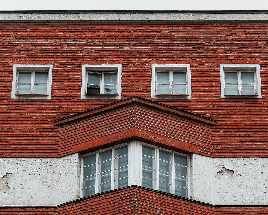 Fassade eines Gebäudes mit roter und weißer Farbe, mit kaputten Fenstern und abblätternden Putz