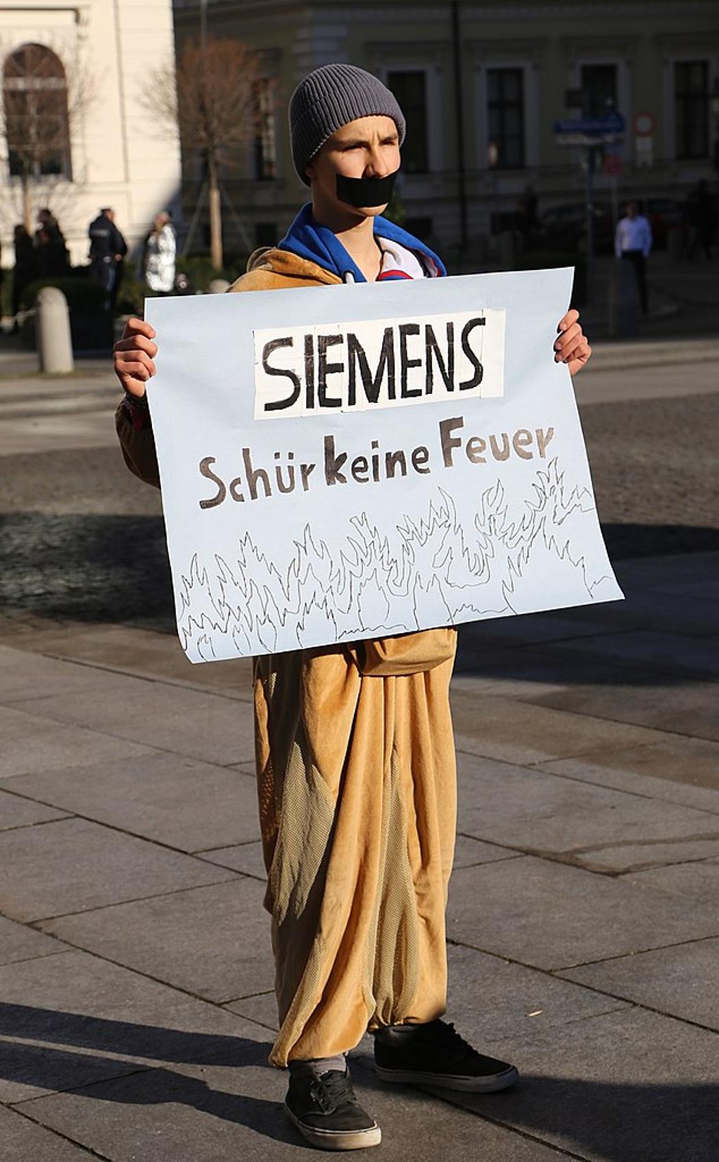 Aktivist von Fridays for Future mit einem Schild, auf dem steht: "Siemens schür keine Feuer"
