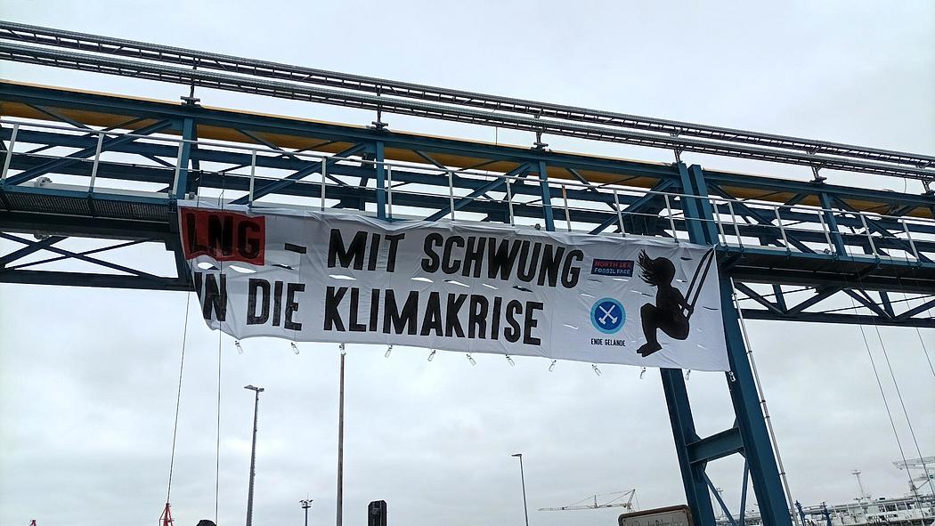 Ein Plakat an einer Pipeline über dem Boden. Darauf steht "LNG - mit Schwung in die Klimakrise"