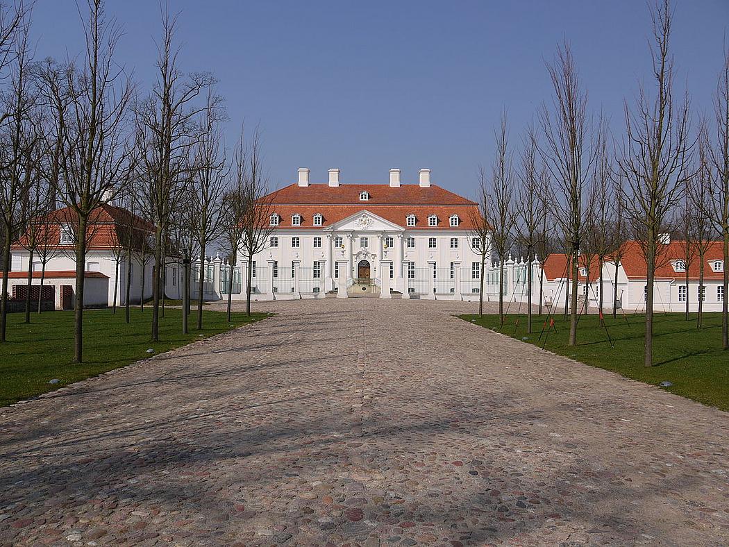 Auffahrt zu einem Schloss mit weißer Fassade und rotem Dach