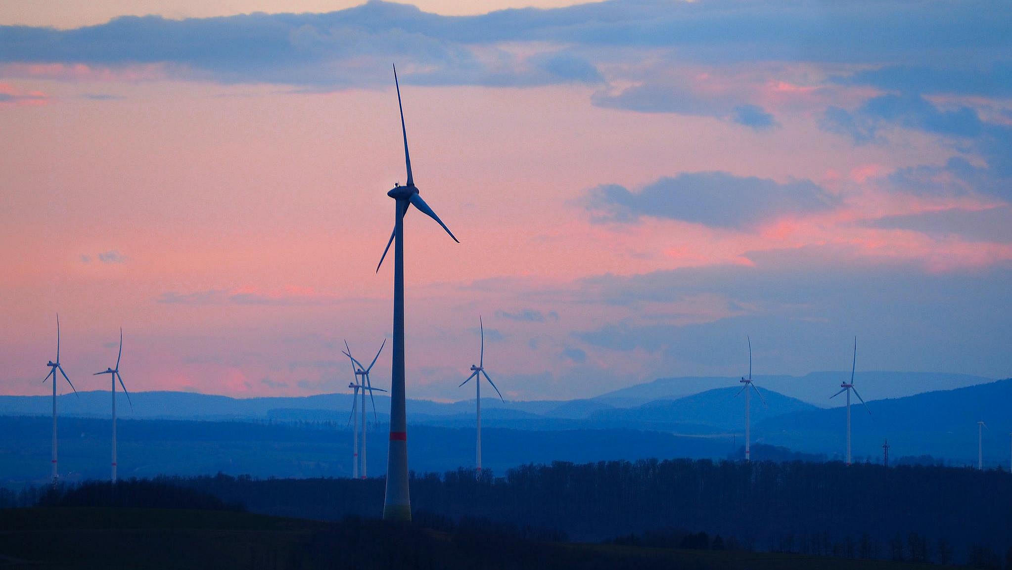 Mehrere Windkrafträder in einer hügeligen Landschaft im Abendrot