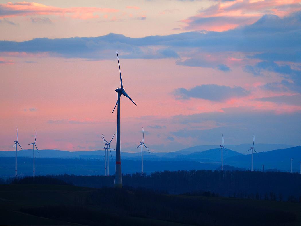Mehrere Windkrafträder in einer hügeligen Landschaft im Abendrot