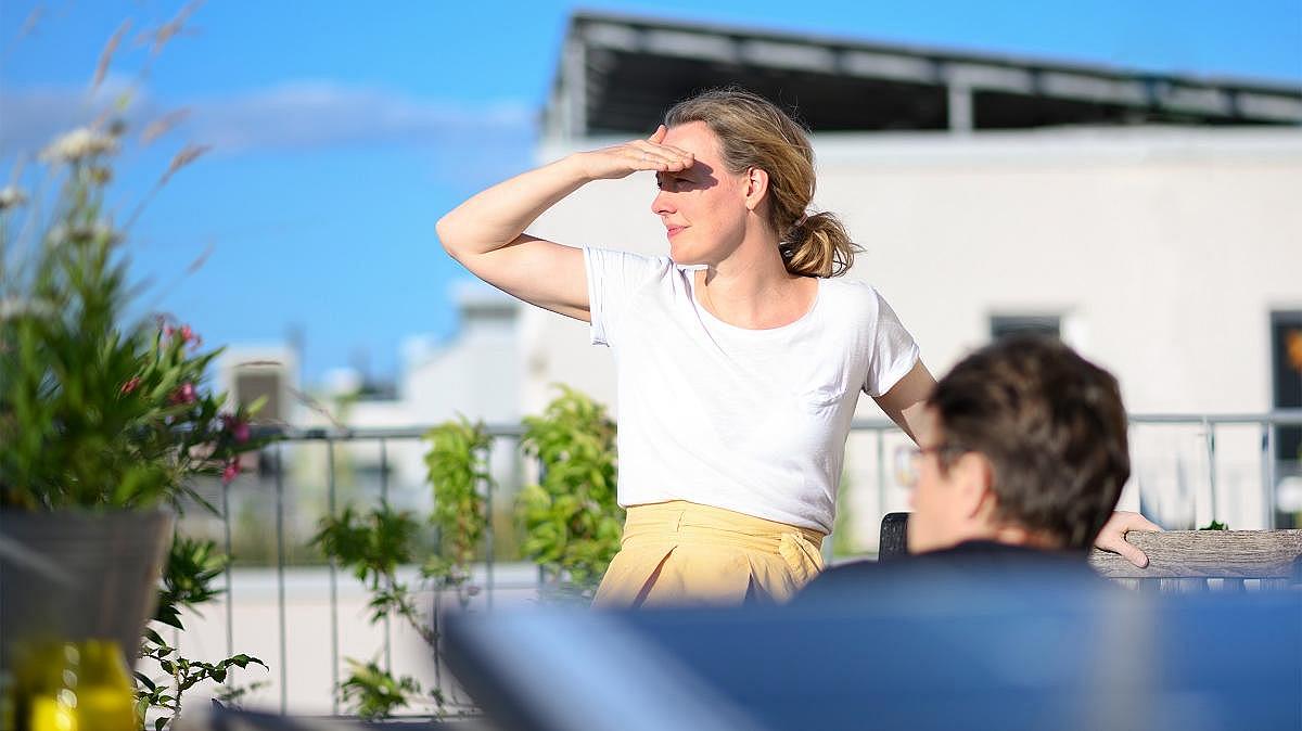 Frau auf einer Dachterrasse mit Photovoltaik-Anlage blickt in die Ferne