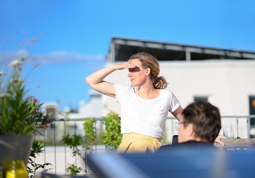 Frau auf einer Dachterrasse mit Photovoltaik-Anlage blickt in die Ferne