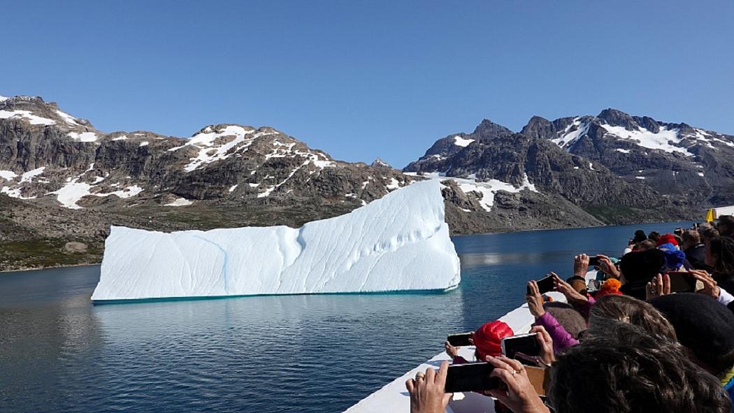 Touristen auf einem Schiff fotografieren mit ihren Smartphones einen kleinen treibenden Eisberg
