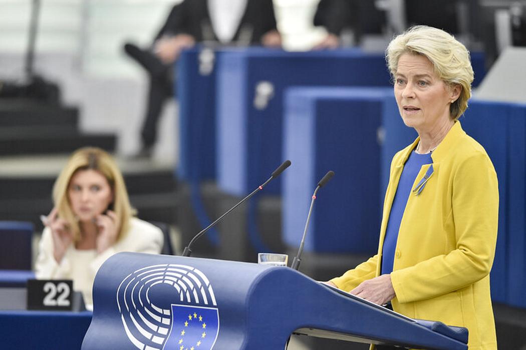 Eine Frau mit blonden Haaren in gelb-blauen Outfit an einem Rednerpult. 