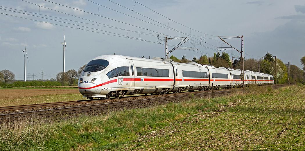 Foto: Ein ICE auf freier Strecke. Im Hintergrund Windkraftanlagen.