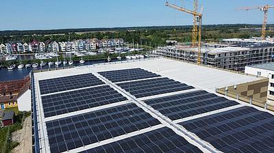 Photovoltaikanlage auf einem Flachdach, im Hintergrund ein Wasserlauf und Häuser