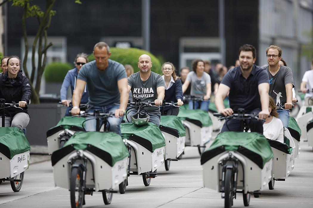 Frauen und Männer fahren auf E-Lastenrädern durch die StadtFrauen und Männer fahren auf E-Lastenrädern durch die Stadt