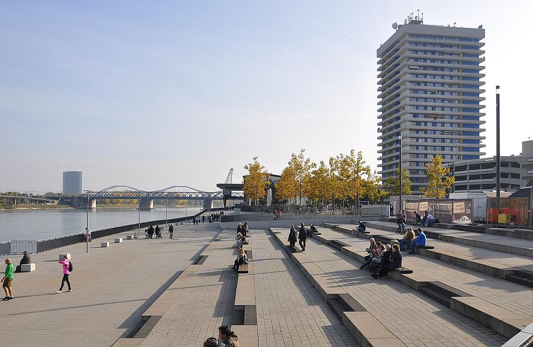 Betontreppe am Ufer eines Flusses, mit Hochhaus im Hintergrund