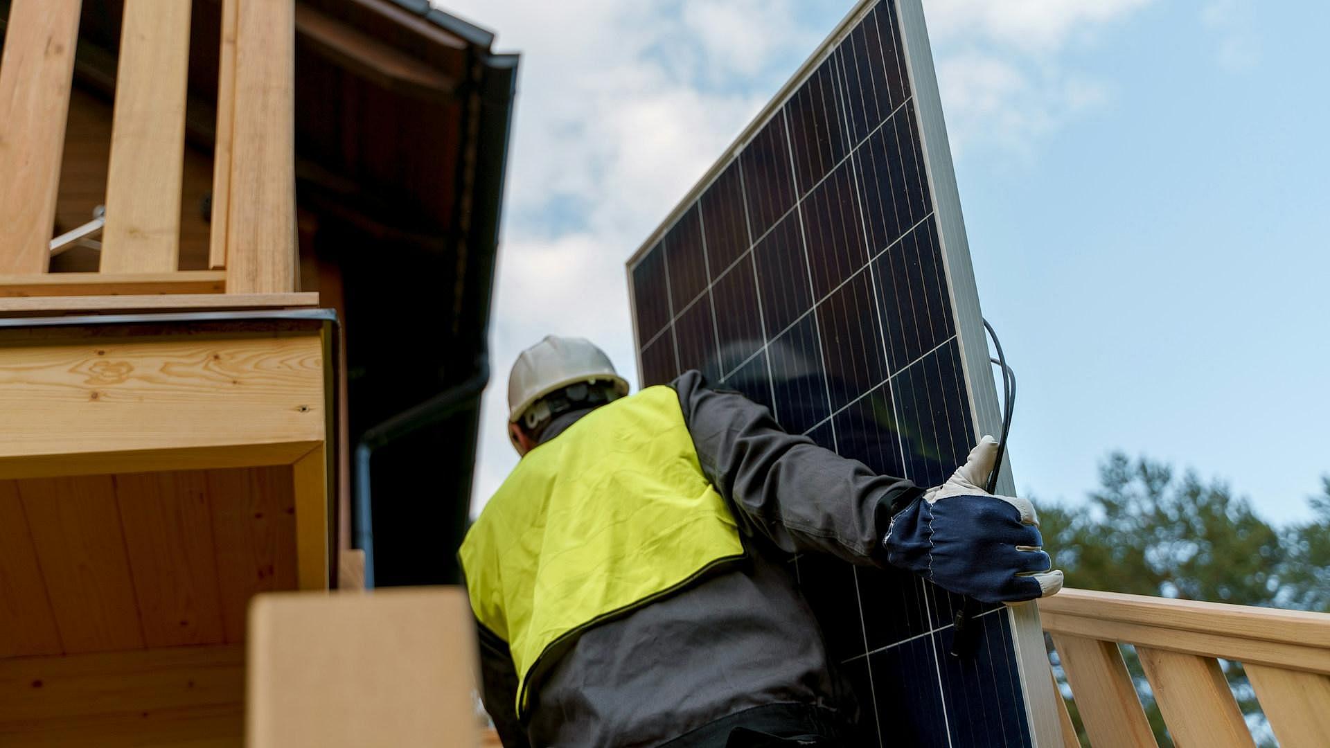 Mann mit Solarpanel vor Haus