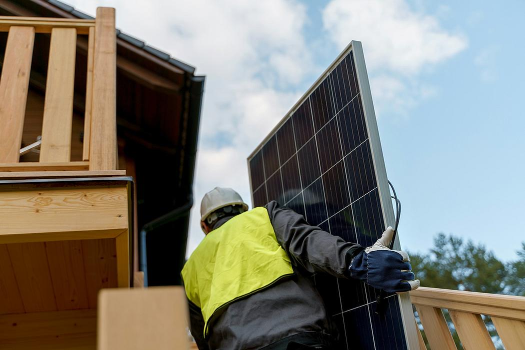 Mann mit Solarpanel vor Haus