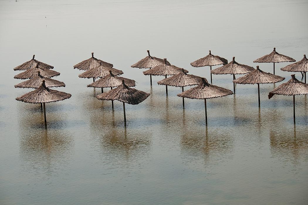 Foto: reedbedeckte Sonnenschirm am Strand, vom Meer überflutet.