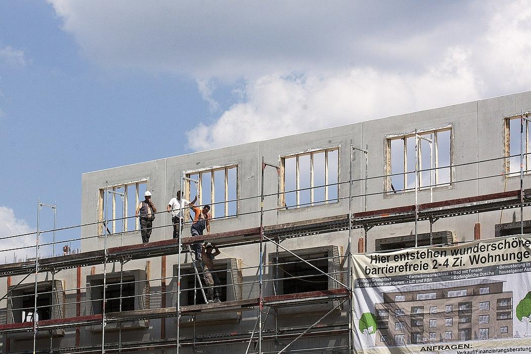 Baustelle mit zwei Bauarbeitern und Werbe-Plakat für Wohnungsneubau