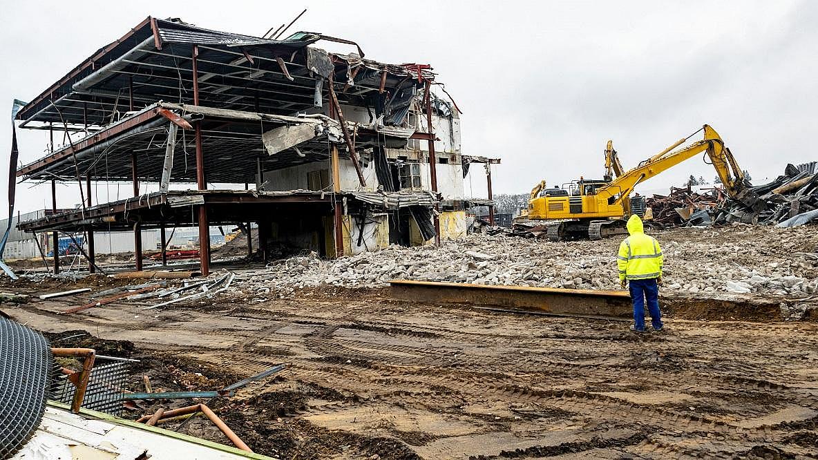 Mann in gelber Arbeitsjacke steht vor einer Abriss-Baustelle