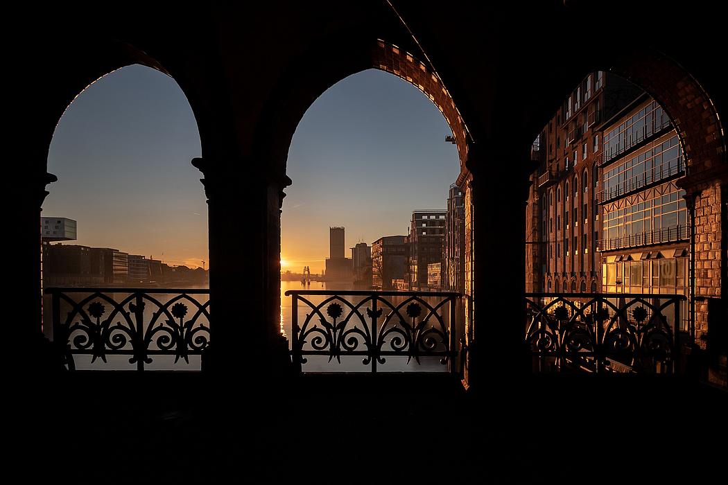 Torbögen einer Brücke, dahinter der Sonnenaufgang