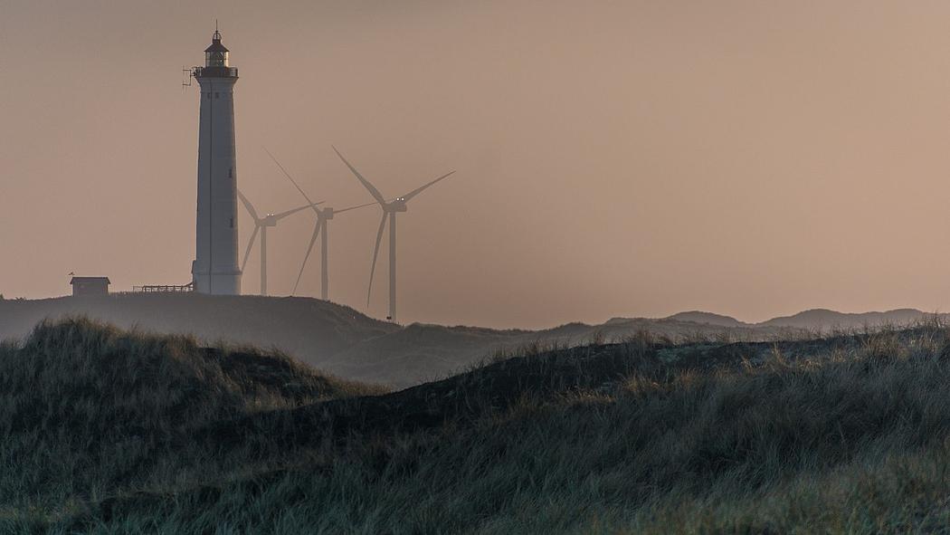 Windenergieanlagen hinter einer Düne und einem Leuchtturm