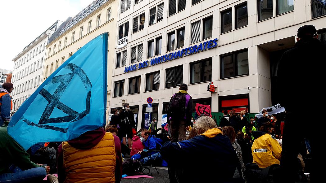 Protest vor dem Wirtschaftsrat der CDU. Sitzende Menschen und Fahnen von Extinction Rebellion