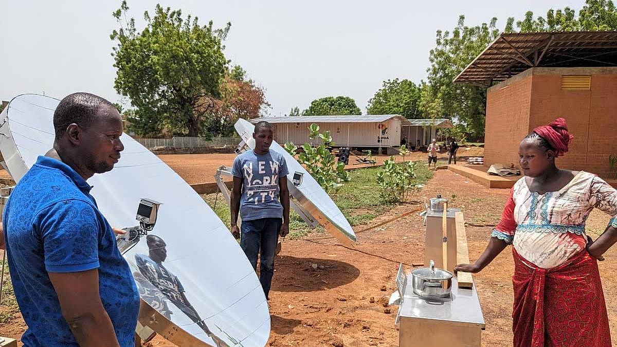 Menschen in Afrika vor solarthermischem Reflektor, im Hintergrund Container mit Photovoltaik