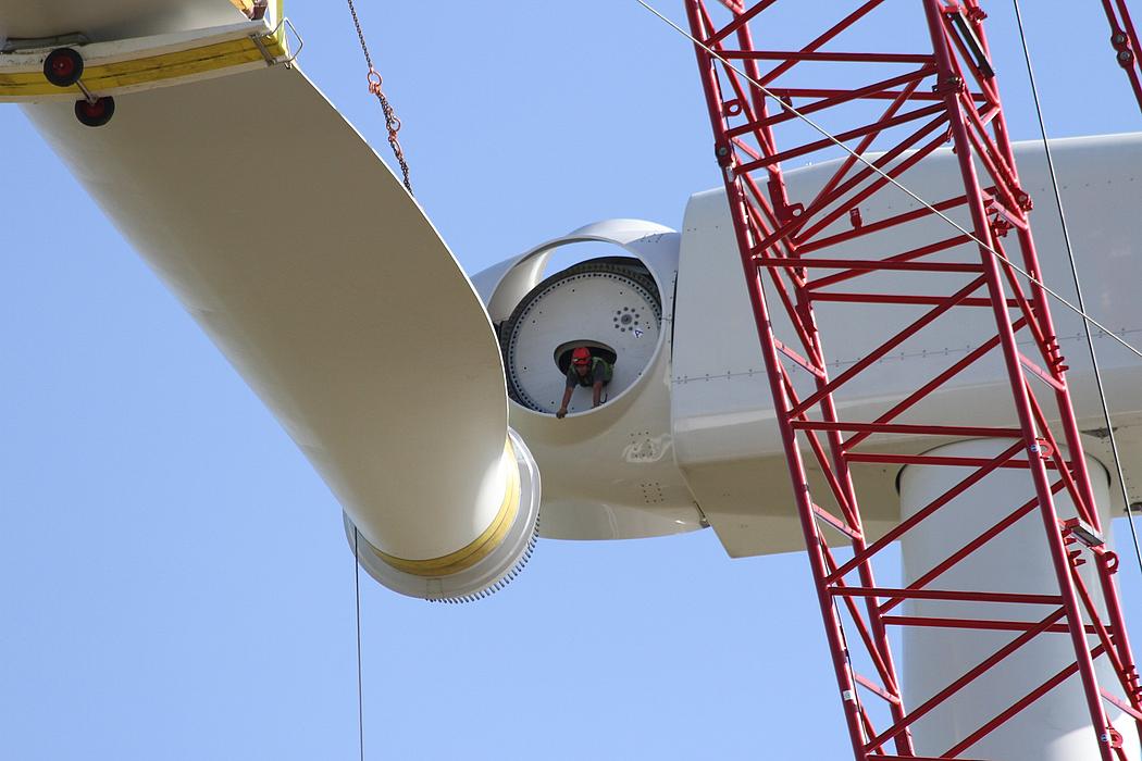 Arbeiter in luftiger Höhe bei Montage eines Windradflügels