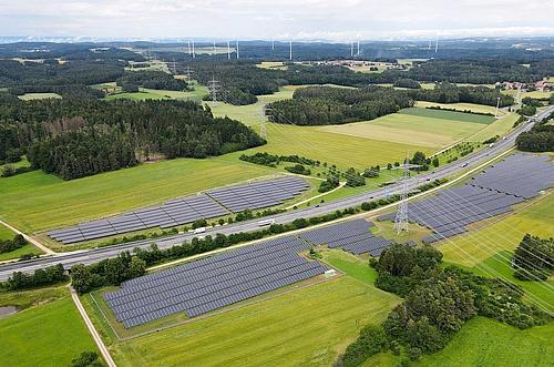 Blick von oben in grüne Landschaft mit Solarpark und dazwischen eine Autobahn