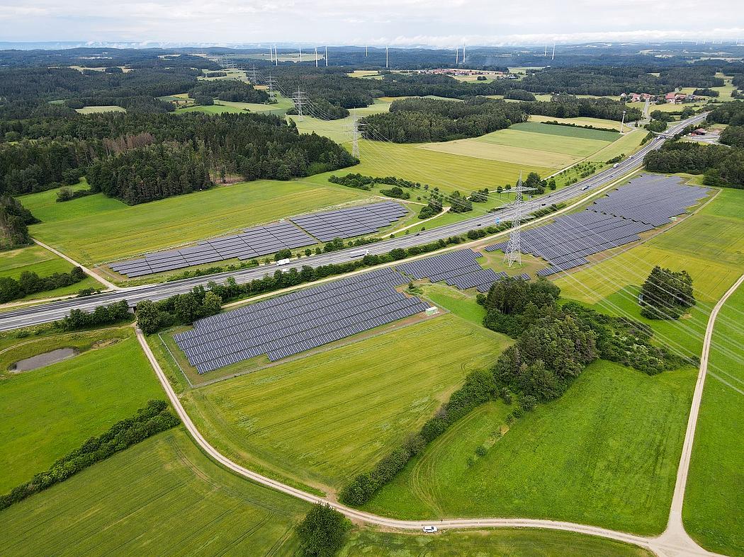 Blick von oben in grüne Landschaft mit Solarpark und dazwischen eine Autobahn