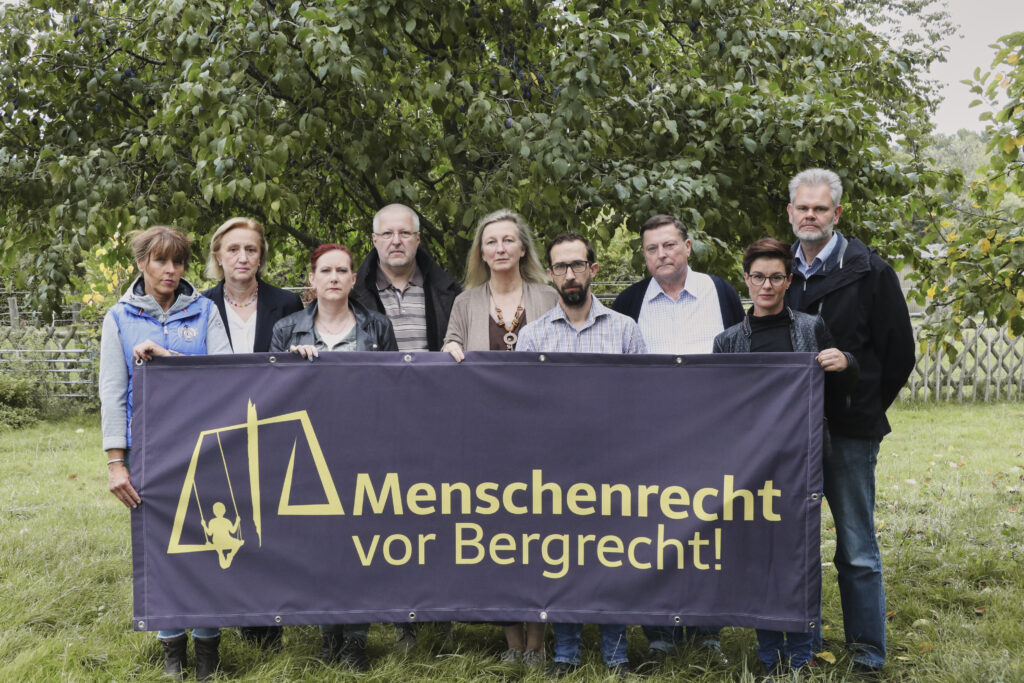 Eine Gruppe von Personen hinter einem Banner, auf dem steht Menschenrecht vor Bergrecht.